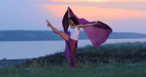 Силуэт девушки танцующей с тканью на траве у реки — стоковое видео