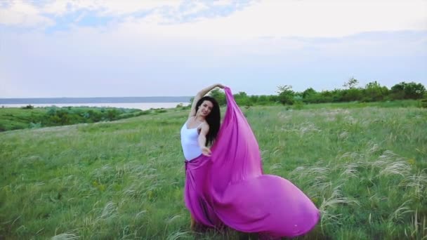 Menina dança segurando chiffon trem em exuberante grama câmera lenta — Vídeo de Stock