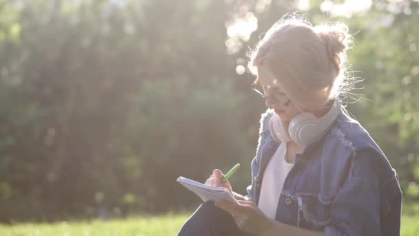 Chica escribe en cuaderno de papel y muestra el pulgar hacia arriba en el parque — Vídeos de Stock