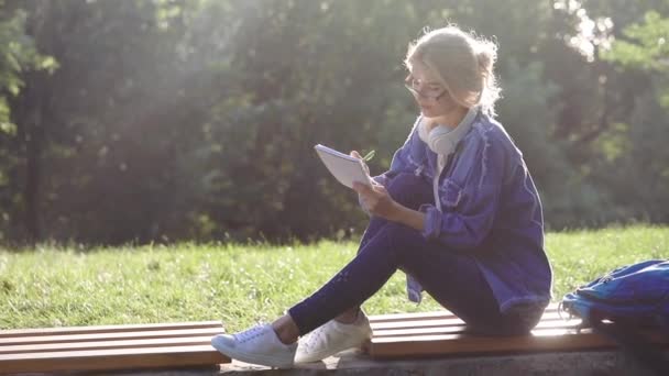 Geïnspireerd blonde in blauwe denim dressing schrijft in notebook — Stockvideo