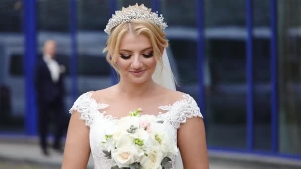 Невеста блондинка с букетом ждет жениха в здании на улице — стоковое видео