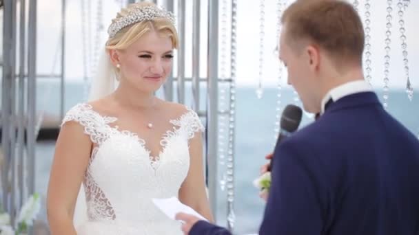 Zwartharige bruidegom spreekt tot blond bruid tegen zee — Stockvideo