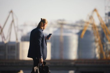 Dans eden işadamı büyük bir fabrikanın arka planında duruyor ve telefonda konuşuyor. İyi haber aldı.