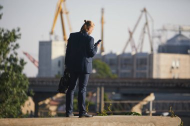 Dans eden işadamı büyük bir fabrikanın arka planında duruyor ve telefonda konuşuyor. İyi haber aldı.