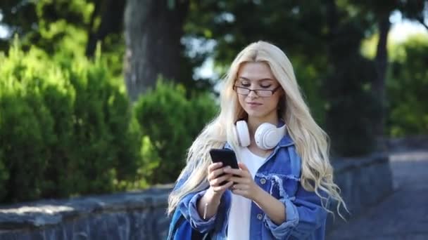 Κομψό Μαθήτρια Κορίτσι Ντένιμ Μπουφάν Smartphone Και Ακουστικά Στο Πάρκο — Αρχείο Βίντεο