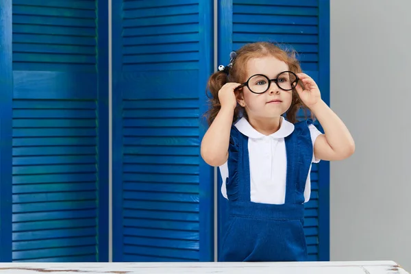 スマート幼児の子供 学校に戻って 幸せな時間 メガネをかけたかわいい勤勉な子供が屋内の机に座っている 子供は青い壁の背景にクラスで学んでいます 本を読んでいる少女 — ストック写真