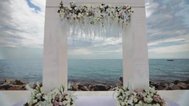 bulutlu gökyüzü altında sahilde taze çiçekler ile düğün kemer