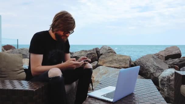 Hombre juega por teléfono con gesto de victoria en la cafetería en la costa del mar — Vídeos de Stock