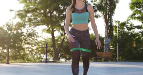 Sportieve dame met paardenstaart praktijken lunges met fitnessband — Stockvideo