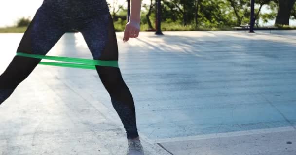 Mulher apto faz costas e laterais lunges com faixa de fitness verde — Vídeo de Stock