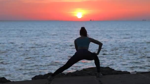 Delgada joven mujer estira las piernas contra el sol de la noche — Vídeos de Stock