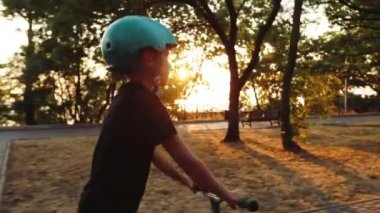 genç adam gün batımında yavaş park döşeli yol boyunca scooter sürmek