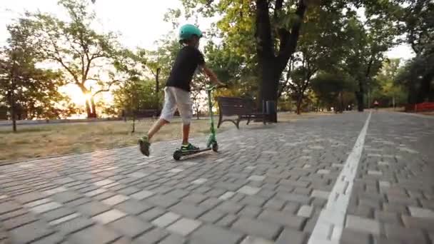 Patinador joven monta scooter a lo largo de verde parque pavimentado carretera — Vídeo de stock