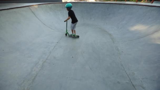 Niño monta scooter a lo largo de la piscina del parque de skate en el día de verano — Vídeos de Stock