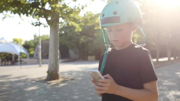 Menino no capacete vagueia no parque e joga no smartphone — Vídeo de Stock