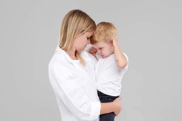 Young mother holding her crying child boy in her arms. The son is ill and feels bad, the woman is sorry for the upset baby