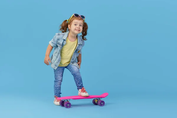青い背景の上にスケートボードを持つスタイリッシュなクールな女の子の子供 — ストック写真