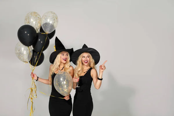 白い背景の上にパーティーに風船と黒の魔女ハロウィーンの衣装を着た2人の幸せな若い女性の肖像画 ハロウィーンの概念 面白い顔 — ストック写真