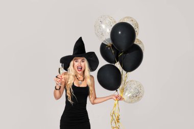 Cadılar Bayramı Partisi kızı. Hava balonları ile Happy Halloween Sexy Witch. Cadılar şapka ve kısa elbise siyah balonlar tutan güzel genç sürpriz kadın. Gri arka planda yalıtılmış.