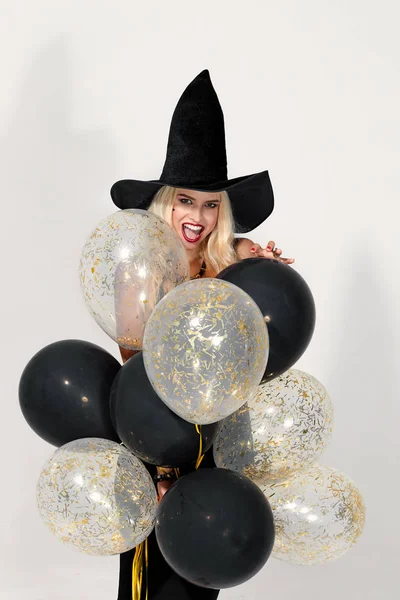 Cadılar Bayramı Partisi kızı. Hava balonları ile Happy Halloween Sexy Witch. Cadılar şapka ve kısa elbise siyah balonlar tutan güzel genç sürpriz kadın. Gri arka planda yalıtılmış.