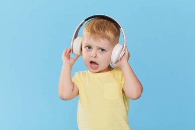 Mutlu gülümseyen çocuk renkli mavi arka plan üzerinde kulaklık müzik dinler sahiptir. Canlı ve eğlenceli duygular, zevkle mutlu çocuk kablosuz kulaklıkşarkıları dinler