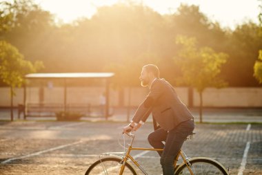 İş elbisesi içinde sakallı Işadamı gün batımında sabah kentsel sokakta çalışmak için retro bisiklet sürme