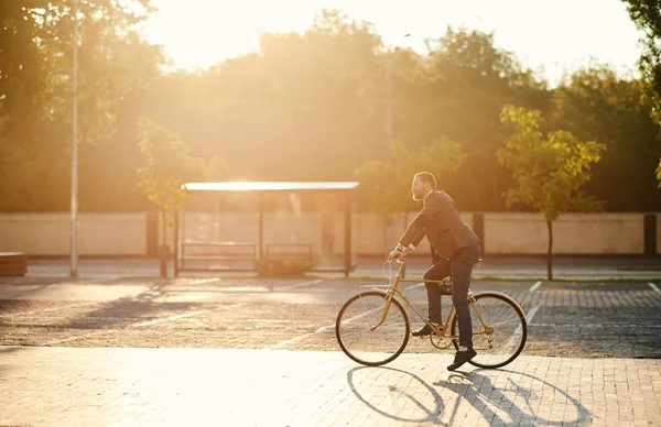 İş elbisesi içinde sakallı Işadamı gün batımında sabah kentsel sokakta çalışmak için retro bisiklet sürme