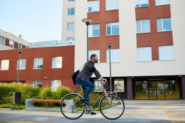 İş elbisesi içinde sakallı Işadamı gün batımında sabah kentsel sokakta çalışmak için retro bisiklet sürme