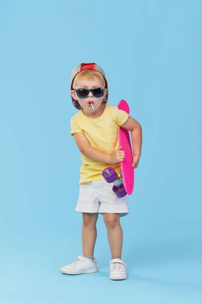 时尚幼儿男孩在眼镜与滑板有乐趣的蓝色背景 — 图库照片