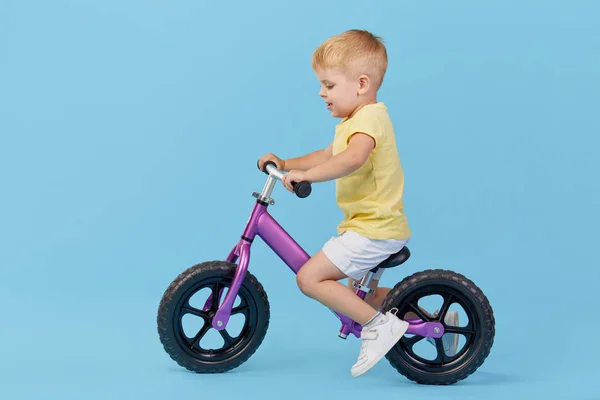 小男孩在骑自行车时学会保持平衡 蓝色背景黄色 恤的时尚儿童 — 图库照片