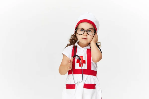 白い背景に聴診器を持って医者の衣装やメガネで幸せなかわいい子供の女の子 彼女の手におもちゃの注射器を保持 予防接種の概念 — ストック写真