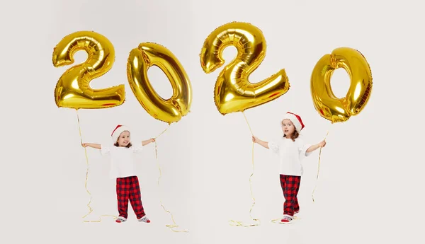 新しい年を祝うサンタの帽子の小さな子供の女の子は2020を迎えます 白い背景に孤立した金色の気球の数の形 クリスマス休暇 — ストック写真