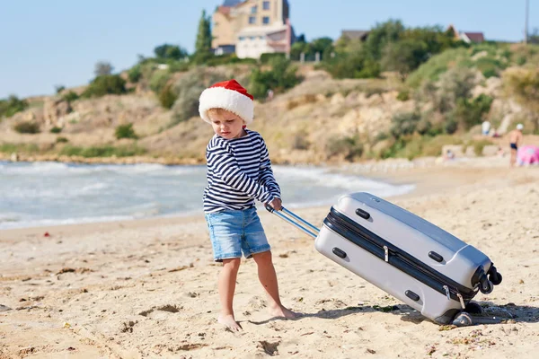 Ein Kleines Kind Mit Weihnachtsmütze Rollt Einen Koffer Tropischen Strand — Stockfoto