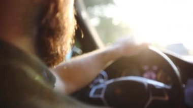 Parlak güneş ışığıyla aydınlatılmış sakallı adam modern arabayı yakınlaştırıyor.