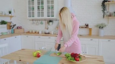 blonde girl in pink warm kigurumi prepares salad in kitchen