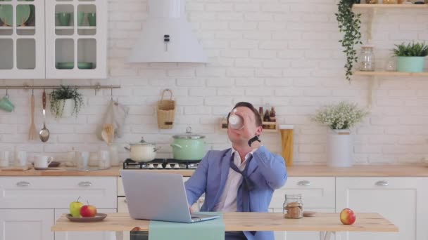 Man in jas werkt op laptop en drinkt koffie in de keuken — Stockvideo