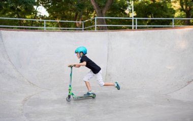 Scooter'lı ve koruyucu kasklı bir çocuk paten parkında inanılmaz gösteriler yapıyor. Aşırı atlayış. Sağlıklı bir yaşam tarzı ve spor eğlence kavramı
