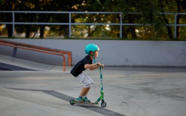Scooter'lı ve koruyucu kasklı bir çocuk paten parkında inanılmaz gösteriler yapıyor. Aşırı atlayış. Sağlıklı bir yaşam tarzı ve spor eğlence kavramı
