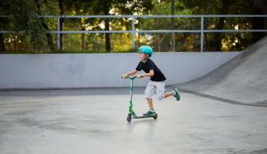 Scooter'lı ve koruyucu kasklı bir çocuk paten parkında inanılmaz gösteriler yapıyor. Aşırı atlayış. Sağlıklı bir yaşam tarzı ve spor eğlence kavramı