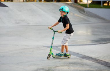 Scooter'lı ve koruyucu kasklı bir çocuk paten parkında inanılmaz gösteriler yapıyor. Aşırı atlayış. Sağlıklı bir yaşam tarzı ve spor eğlence kavramı