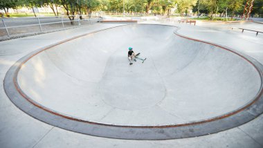 Uzun bir motosiklet egzersizinden sonra kaykay parkında yerde oturan yorgun çocuk.