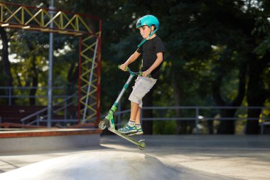 Scooter'lı ve koruyucu kasklı bir çocuk paten parkında inanılmaz gösteriler yapıyor. Aşırı atlayış. Sağlıklı bir yaşam tarzı ve spor eğlence kavramı