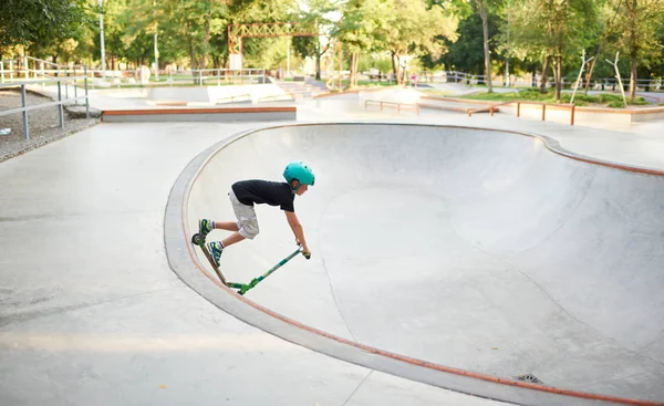 A boy on a scooter and in protective helmet do incredible stunts in skate park. Extreme jump. The concept of a healthy lifestyle and sports leisure