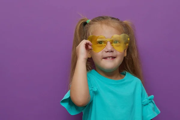 紫の背景に隔離された薄着と眼鏡を身に着けている小さな幼児の子供の少女の肖像画 顔の近くに手を握って幸せな子供時代 すごいと衝撃的なコンセプト — ストック写真
