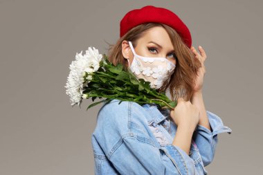Çiçekli koronavirüs salgını karantinası sırasında moda kıyafetli bir kadın. Model kıyafetleri, el yapımı maskeler ve kırmızı bereler.