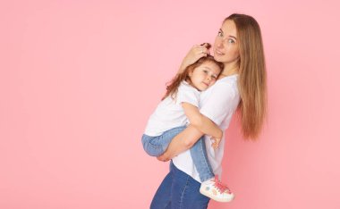 Beyaz tişörtlü ve kot pantolonlu anne ve kız pembe arka planda oynaşıp sarılıyorlar. Sevdiklerinle ilgilenmek. Mutlu annelik