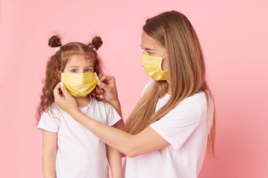 Sevdiklerinle ilgilenmek. Genç anne Covid-19 salgını sırasında koruyucu tıbbi maskeler takan küçük kıza sarılıyor. Stüdyo pembe arkaplan