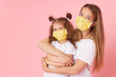 Sevdiklerinle ilgilenmek. Genç anne Covid-19 salgını sırasında koruyucu tıbbi maskeler takan küçük kıza sarılıyor. Stüdyo pembe arkaplan