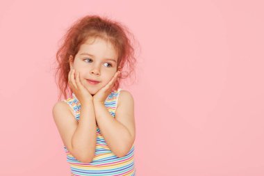 Pembe arka planda küçük şirin bir kızın şaşırmış portresi. Kameraya bakıyorum. Sol tarafı işaret eden eller. Çocuk ürünlerinin reklamını yapmak