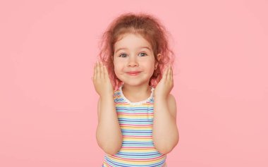 Pembe arka planda küçük şirin bir kızın şaşırmış portresi. Kameraya bakıyorum. Sol tarafı işaret eden eller. Çocuk ürünlerinin reklamını yapmak